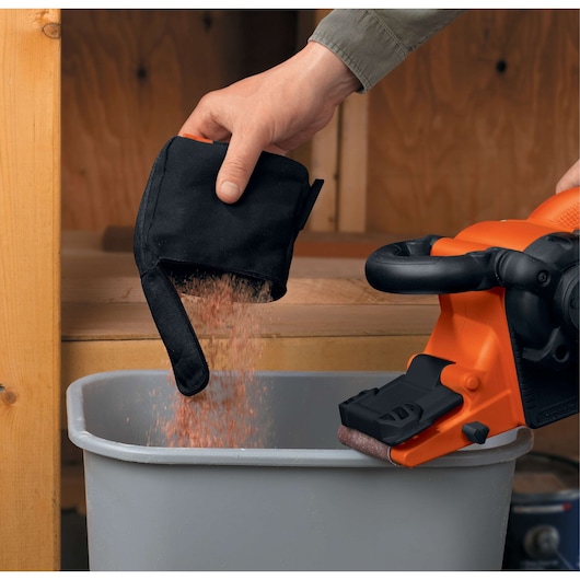 Photo of BLACKDECKER DS321 sander being emptied as a hand pours dust from the dust bag into a trash bin.