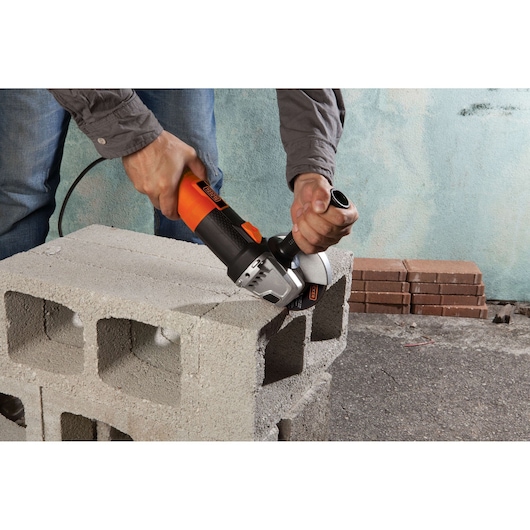 Photo of BLACKDECKER G720 angle grinder used to cut a concrete block, showing tool in operation.