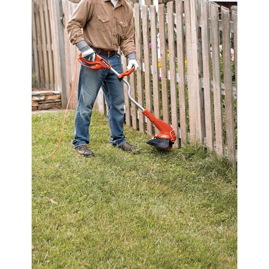 BLACKDECKER GH750 electric string trimmer used on grass near a wooden fence in outdoor yard.