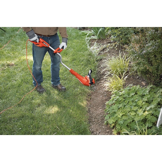 Person using BLACKDECKER GH750 string trimmer for lawn edging near garden beds outdoors.