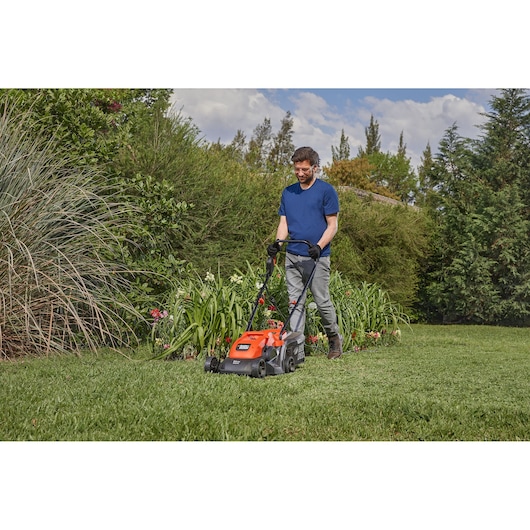 Photo of a person using a BLACKDECKER GR3400 lawn mower on grass with bushes and flowers in the background.