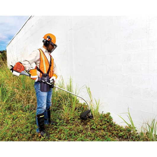 BLACKDECKER GST26 grass trimmer in use outdoors by worker with safety gear near white wall.