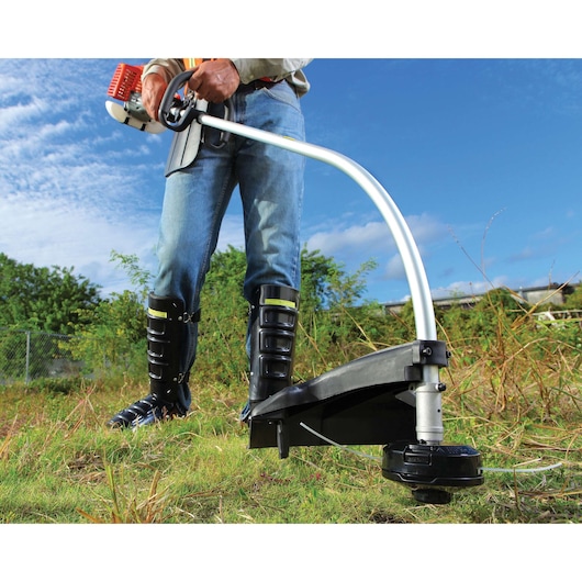 BLACKDECKER GST26 grass trimmer, close-up outdoor view, person holding handle, wearing protective boots.