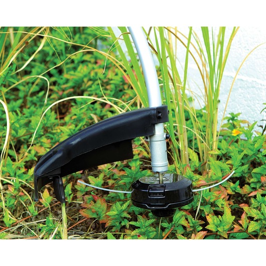 BLACKDECKER GST26 grass trimmer head cutting green weeds in a garden, close-up view.