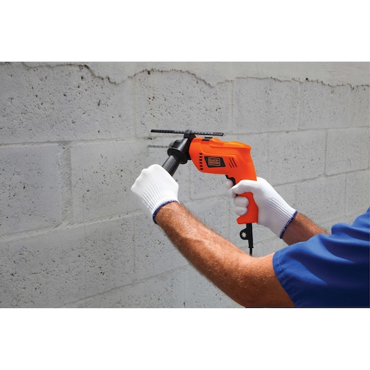 BLACKDECKER HD555 orange hammer drill in use on concrete wall, handled by person wearing white gloves.