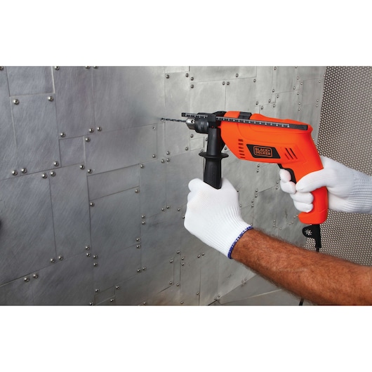 Photo of BLACKDECKER HD650 orange corded drill with side handle drilling into metal wall.