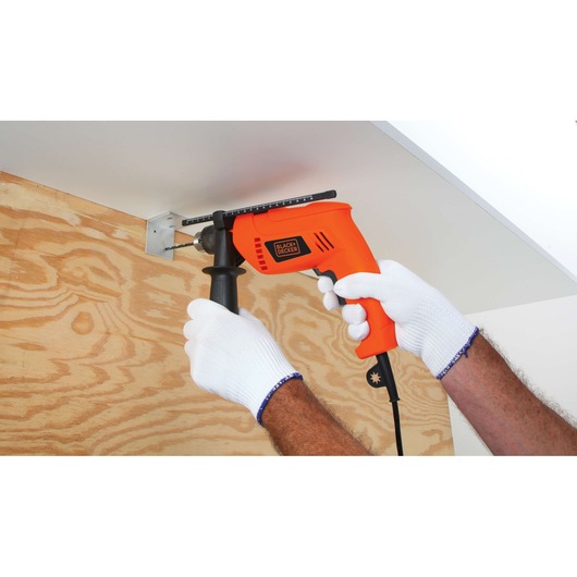 BLACKDECKER HD650 orange corded drill in use on wood with auxiliary handle, close-up photography.