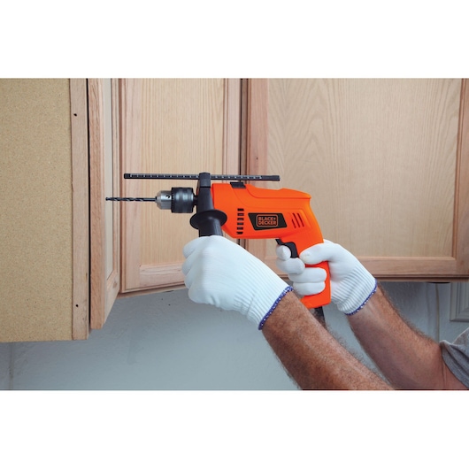 Photo of BLACKDECKER HD650 orange corded drill in use drilling into wooden cabinet, gloved hands holding.