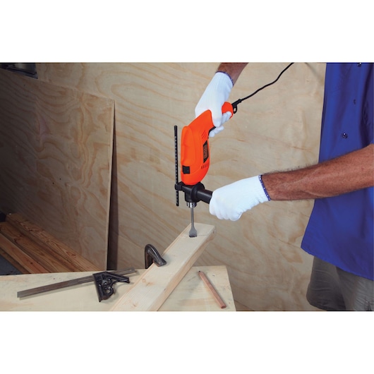 BLACKDECKER HD650 electric drill used to bore a hole in a wooden beam, person wearing white gloves.