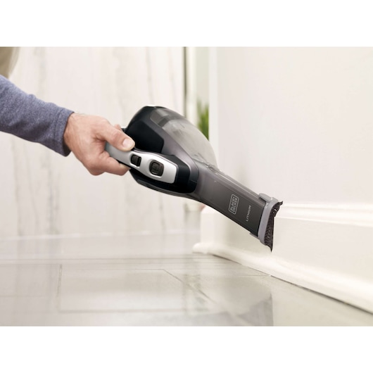 BLACKDECKER HLVA320J00 handheld vacuum cleaning along a baseboard on a tile floor, close-up view.