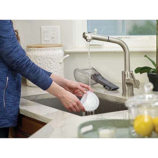 BLACKDECKER HLVA320J00 handheld vacuum filter being rinsed under a kitchen faucet with vacuum on counter.