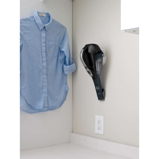 BLACKDECKER HLVA320J00 handheld vacuum mounted on wall near light blue shirt, photography showing laundry room.