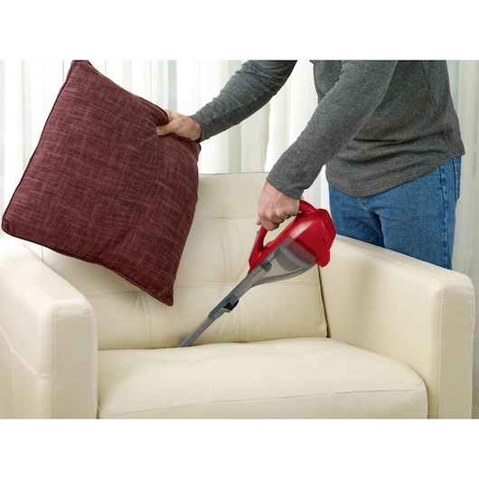 BLACKDECKER HLVA320J26 handheld vacuum cleaning a cream sofa with a red cushion lifted.