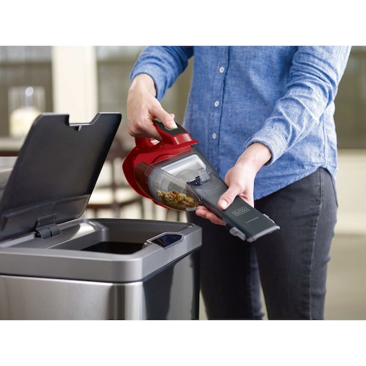BLACK+DECKER HLVA320J26 handheld vacuum being emptied into a trash can, person holding the vacuum.