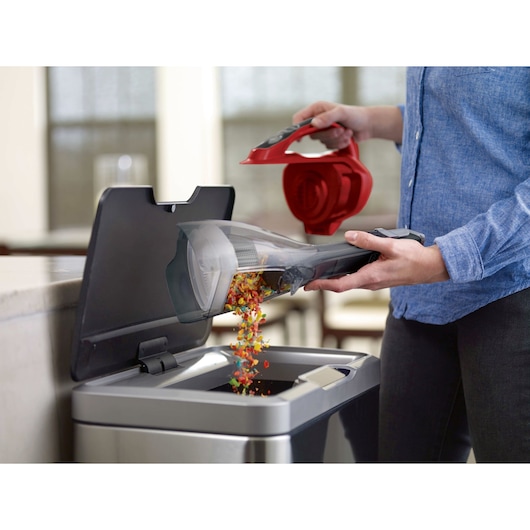 BLACKDECKER HLVA320J26 handheld vacuum being emptied into a trash can, person removing red filter.