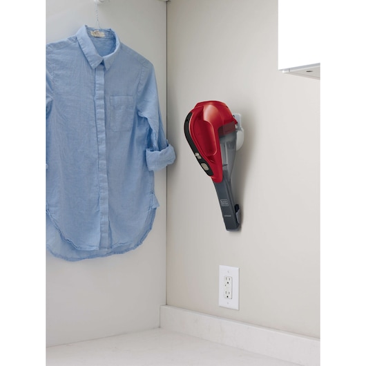 BLACKDECKER HLVA320J26 handheld vacuum red and gray, wall-mounted near blue shirt.