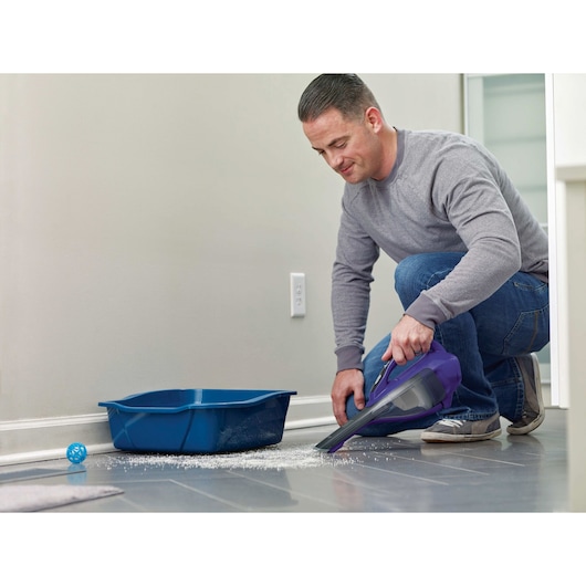 BLACKDECKER HLVA325JP07 handheld vacuum cleaning spilled litter near a blue cat box on tile floor.