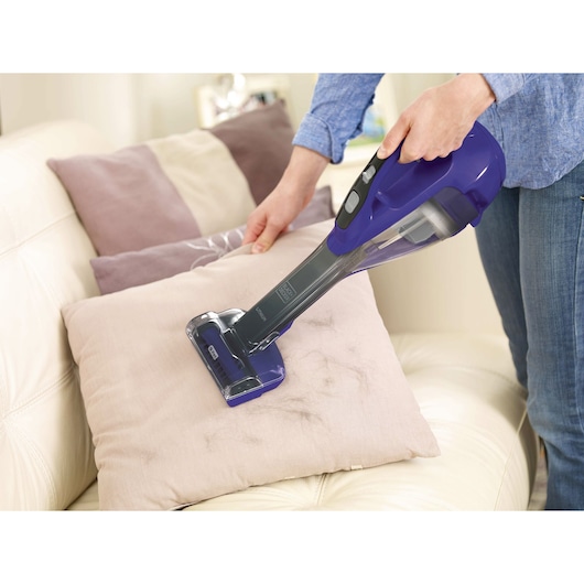 BLACKDECKER HLVA325JP07 handheld vacuum cleaning a beige pillow on a sofa.
