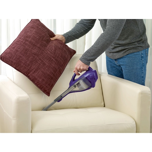 BLACKDECKER HLVA325JP07 handheld vacuum cleaning cream armchair under red cushion.