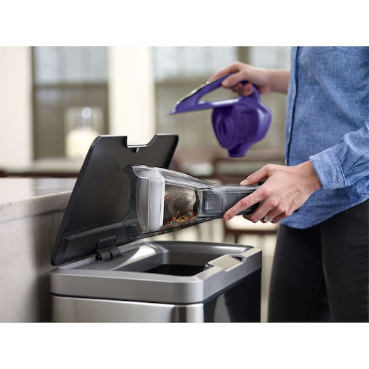 BLACKDECKER HLVA325JP07 handheld vacuum being emptied into a kitchen trash bin.