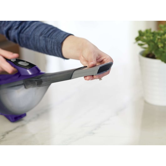 Photo of BLACKDECKER HLVA325JP07 handheld vacuum with person using narrow nozzle on countertop.