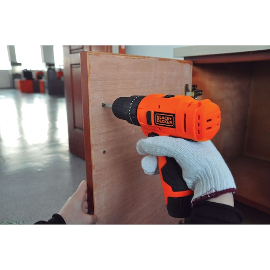Photo of BLACK+DECKER HP12 orange cordless drill being used to assemble a wooden cabinet.