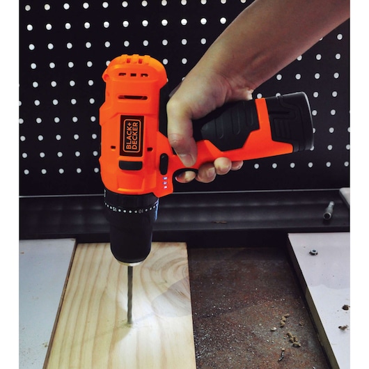 BLACK+DECKER HP12 cordless drill in use on wood surface, close-up side view.