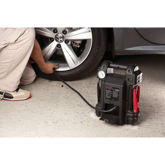 BLACKDECKER JS350CC portable jump starter inflating a car tire, pressure gauge and cables visible.