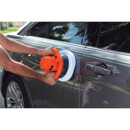 BLACK+DECKER KP12K orange car polisher being used to polish a gray car door outdoors.