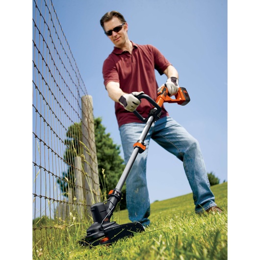 Photo of BLACKDECKER LST136 cordless string trimmer in use cutting grass near a wire fence outdoors.