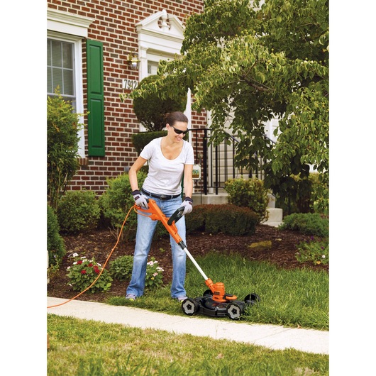 BLACKDECKER MTE912 corded lawn mower in use on grass near a sidewalk outside a brick house.