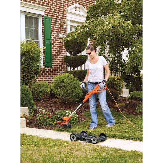BLACKDECKER MTE912 lawn trimmer and mower in use by a person on a residential lawn, outdoor angle.
