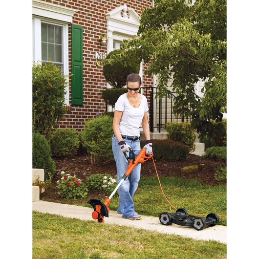 BLACKDECKER MTE912 corded lawn trimmer used outdoors near a garden sidewalk with orange and black design.