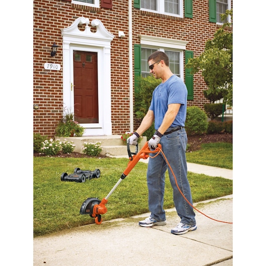 BLACK+DECKER MTE912 lawn trimmer in use on grass lawn in front of brick house, outdoor photography.