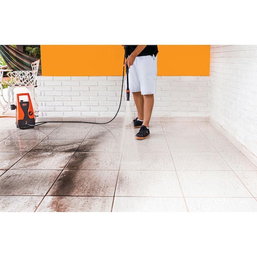 BLACKDECKER PW1450TD pressure washer cleaning dirty tiles, side view of orange and white unit in use.