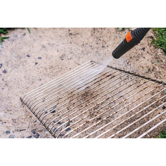 BLACKDECKER PW1450TD pressure washer cleaning a metal grill on a stone surface.