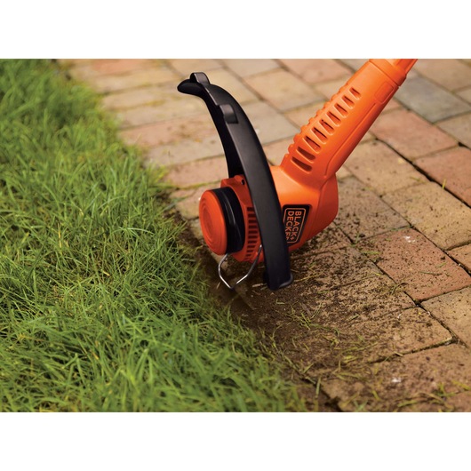 BLACKDECKER ST7700 orange string trimmer edging green grass along brick walkway, close-up.