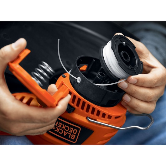 BLACKDECKER ST7700 string trimmer spool installation, close-up of hands with orange and black housing.