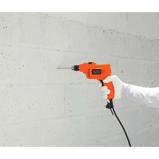 Photo of BLACK+DECKER TP550 orange electric drill in use against a white concrete wall.