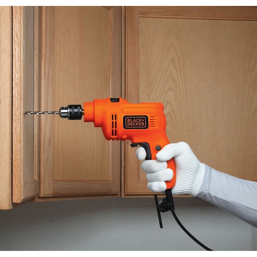 BLACKDECKER TP555 corded orange electric drill held by gloved hand, drilling into wood cabinet.